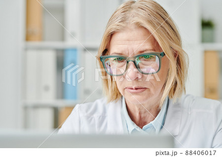 Contemporary mature online doctor looking at computer screen in office 88406017