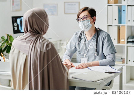 Contemporary doctor in protective mask talking to female patient in hijab Contemporary doctor in protective mask talking to female patient in hijab 88406137