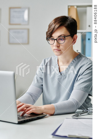 Young doctor in eyeglasses and medical uniform consulting patients online Young doctor in eyeglasses and medical uniform consulting patients online 88406188
