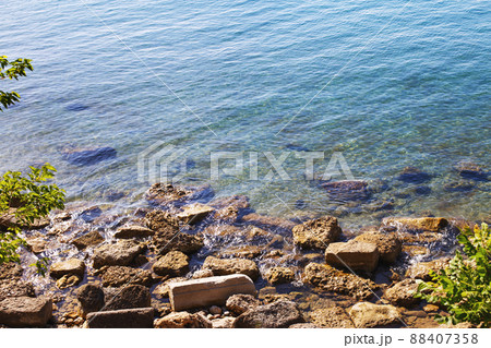 Blue water background with stones and green grass on the shore. sea, river, lake or ocean surface close 88407358