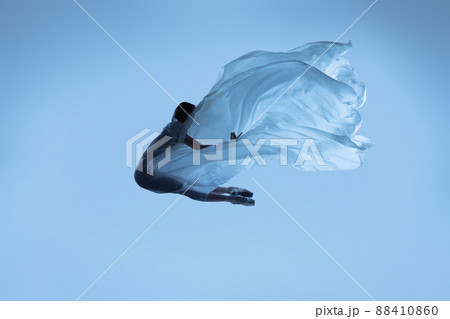 Portrait of flexible woman, graceful ballerina dancing with fabric, cloth isolated on blue studio background. Grace, art, beauty concept. Weightless, tenderness. 88410860