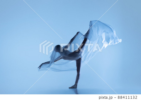 Portrait of flexible woman, graceful ballerina dancing with fabric, cloth isolated on blue studio background. Grace, art, beauty concept. Weightless, tenderness. Portrait of flexible woman, graceful ballerina dancing with fabric, cloth isolated on blue studio background. Grace, art, beauty concept. Weightless, tenderness. 88411132