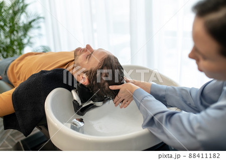 Beautician washing hair to the client and massaging his head 88411182