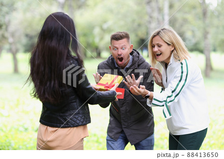 Woman opens gift box and couple looks on happily Woman opens gift box and couple looks on happily 88413650