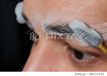 Professional barber doing threading procedure and correcting shape of eyebrows to young male client with tweezer in barber shop. Barber at work. Brow care concept. Plucking brows. 88414162