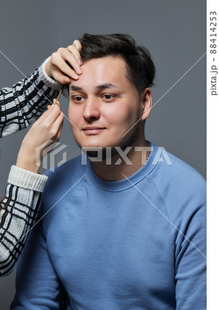 Professional barber doing threading procedure and correcting shape of eyebrows to young male client with tweezer in barber shop. Barber at work. Brow care concept. Plucking brows. Professional barber doing threading procedure and correcting shape of eyebrows to young male client with tweezer in barber shop. Barber at work. Brow care concept. Plucking brows. 88414253