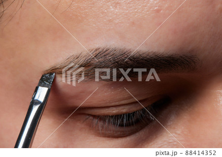 Professional barber doing threading procedure and correcting shape of eyebrows to young male client with tweezer in barber shop. Barber at work. Brow care concept. Plucking brows. 88414352