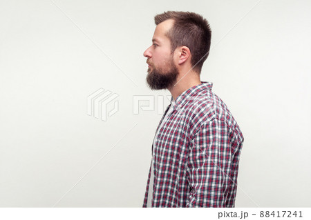 Side view portrait of serious bearded young man in plaid shirt standing looking with calm confident expression, empty place for ad text, copy space. indoor studio shot isolated on white background Side view portrait of serious bearded young man in plaid shirt standing looking with calm confident expression, empty place for ad text, copy space. indoor studio shot isolated on white background 88417241