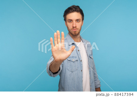 Prohibition, denied access. Portrait of serious man in worker denim shirt doing stop sign with palm of hand, warning expression with negative gesture. indoor studio shot isolated on blue background 88417394