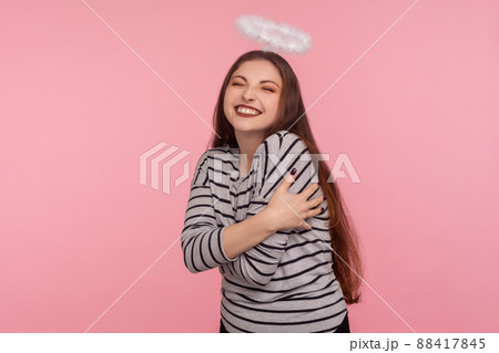 I love myself. Portrait of optimistic attractive happy woman with holy nimbus over head embracing herself and smiling carefree, positive self-esteem concept. studio shot isolated on pink background I love myself. Portrait of optimistic attractive happy woman with holy nimbus over head embracing herself and smiling carefree, positive self-esteem concept. studio shot isolated on pink background 88417845