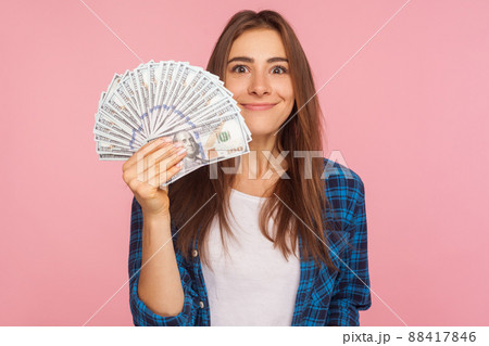 Portrait of happy lucky girl in checkered shirt holding lot of money and smiling to camera, showing dollar bills in hand, enjoying financial success. indoor studio shot isolated on pink background Portrait of happy lucky girl in checkered shirt holding lot of money and smiling to camera, showing dollar bills in hand, enjoying financial success. indoor studio shot isolated on pink background 88417846