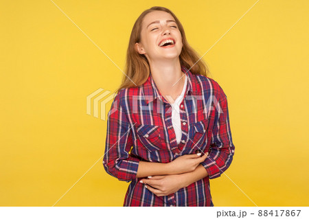 Portrait of carefree ginger girl in checkered shirt holding belly and laughing out loud after hearing hilarious joke, funny anecdote, being in good mood. studio shot isolated on yellow background Portrait of carefree ginger girl in checkered shirt holding belly and laughing out loud after hearing hilarious joke, funny anecdote, being in good mood. studio shot isolated on yellow background 88417867