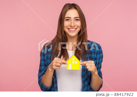 Buying property. Cheerful smiling girl in checkered shirt pleased with house bought, holding paper home and smiling, profitable mortgage for young people. studio shot isolated on a pink background. 88417922