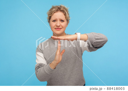 Frustrated woman with short curly hair in grey sweatshirt feeling tired and overworked, showing timeout gesture, need more time, missing deadline. indoor studio shot isolated on blue background Frustrated woman with short curly hair in grey sweatshirt feeling tired and overworked, showing timeout gesture, need more time, missing deadline. indoor studio shot isolated on blue background 88418003