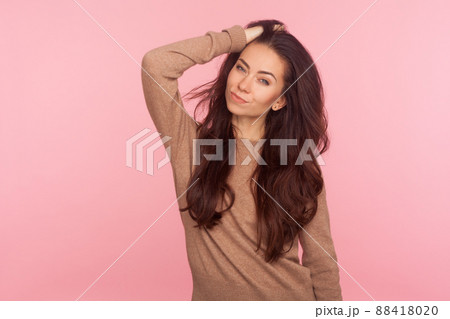 Portrait of stunning sexy slim woman in casual pullover touching her long brunette wavy hair and looking at camera with alluring eyes, fashion and beauty concept. indoor studio shot, pink background Portrait of stunning sexy slim woman in casual pullover touching her long brunette wavy hair and looking at camera with alluring eyes, fashion and beauty concept. indoor studio shot, pink background 88418020