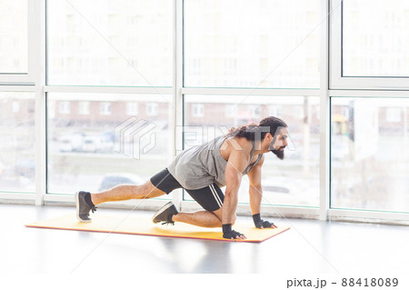 Portrait of handsome young adult muscular man with curly long hair in sportswear on yellow mat doing abs exercise to tone stomach muscles. Indoor, window background, sport and healthy concept Portrait of handsome young adult muscular man with curly long hair in sportswear on yellow mat doing abs exercise to tone stomach muscles. Indoor, window background, sport and healthy concept 88418089