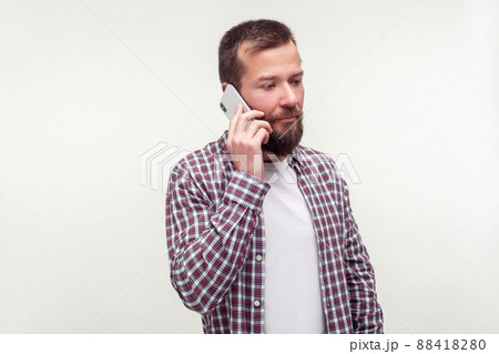 Portrait of serious upset bearded man in plaid shirt talking on cell phone, looking aside with gloomy dismal face, bad news, mobile communication. indoor studio shot isolated on white background 88418280