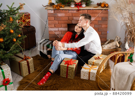 A couple in love are sitting on the floor and flirting. Decorated Christmas tree for Christmas. A unique Christmas atmosphere. 88420099