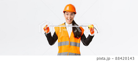 Excited and upbeat asian female construction engineer measuring layout, holding tape measure and smiling, ready for work at build something, standing over white background in safety helmet Excited and upbeat asian female construction engineer measuring layout, holding tape measure and smiling, ready for work at build something, standing over white background in safety helmet 88420143