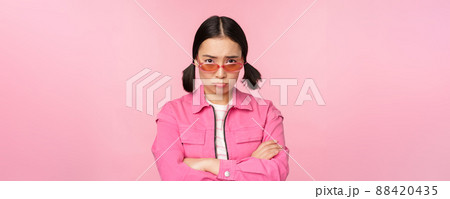 Portrait of sad and gloomy asian girl sulking from disappointment, standing upset against pink studio background Portrait of sad and gloomy asian girl sulking from disappointment, standing upset against pink studio background 88420435