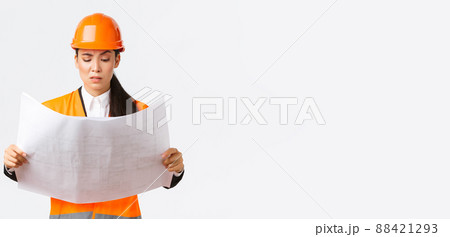 Confused and doubtful asian female chief engineer, lead architect at construction area looking displeased and hesitant at strange blueprints, reading confusing building project, white background Confused and doubtful asian female chief engineer, lead architect at construction area looking displeased and hesitant at strange blueprints, reading confusing building project, white background 88421293