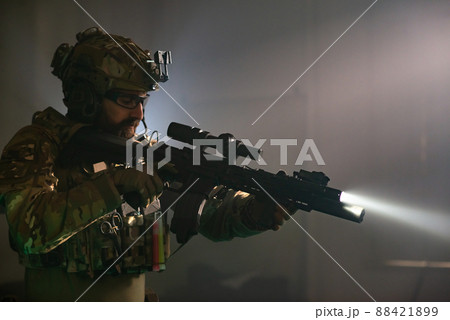 Absorbed bearded man in military equipment in dark room Absorbed bearded man in military equipment in dark room 88421899