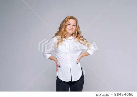 Smiling young blonde woman in white shirt posing isolated on gray walls 88424066