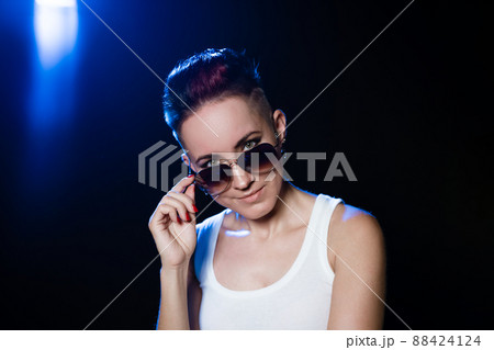 Happy woman in glasses with short hair touches round sunglasses with her hands 88424124