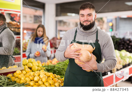 Portrait of positive man in apron selling small decorative pumpkins 88427345