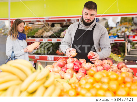 Positive man in apron selling ripe pomegranates 88427421