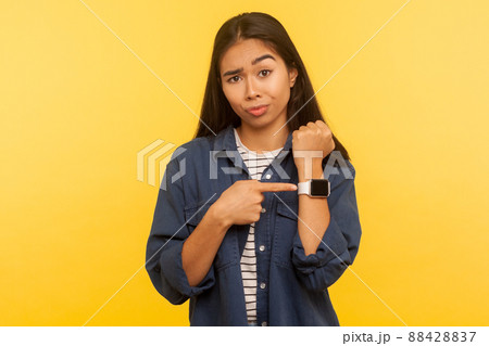 Time to go, hurry up. Portrait of displeased angry woman in denim shirt looking impatient and pointing wristwatch, warning of deadline, late hour. indoor studio shot isolated on yellow background Time to go, hurry up. Portrait of displeased angry woman in denim shirt looking impatient and pointing wristwatch, warning of deadline, late hour. indoor studio shot isolated on yellow background 88428837