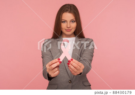 Female health, medical insurance. Portrait of young positive businesswoman in elegant suit jacket holding pink ribbon, warning of breast cancer risk and society awareness. studio shot, pink background 88430179
