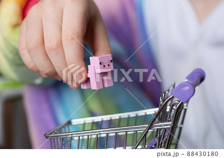 Close-up of children's hands. The child, during the game, puts the pig figurine in a shopping basket. The concept of buying pork 88430180