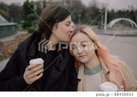 Young ukrainian lesbian couple kissing each other at the street with coffee Young ukrainian lesbian couple kissing each other at the street with coffee 88430933