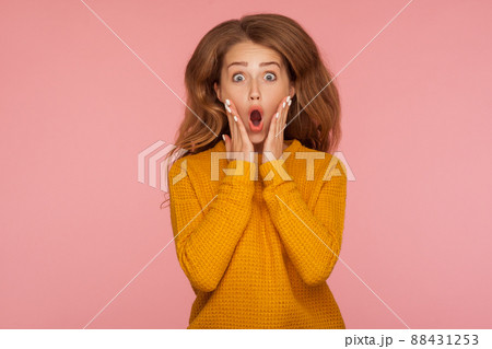 Portrait of extremely excited shocked ginger girl in sweater jumping and holding hands on cheeks and screaming in amazement surprise, her hair flying up. indoor studio shot isolated on pink background Portrait of extremely excited shocked ginger girl in sweater jumping and holding hands on cheeks and screaming in amazement surprise, her hair flying up. indoor studio shot isolated on pink background 88431253