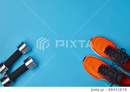 Orange sneakers and metal dumbbells on a blue background 88431678