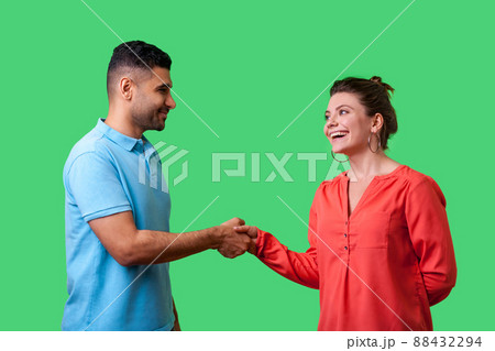 Nice to meet you. Portrait of happy young couple in casual wear standing, smiling at each other and shaking hands, friendly meeting or acquaintance. isolated on green background, indoor studio shot Nice to meet you. Portrait of happy young couple in casual wear standing, smiling at each other and shaking hands, friendly meeting or acquaintance. isolated on green background, indoor studio shot 88432294