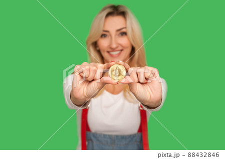 Look at digital money. Portrait of happy adult blond woman with charming smile holding golden bitcoin, showing btc coin and expressing optimism, joy. indoor studio shot isolated on green background Look at digital money. Portrait of happy adult blond woman with charming smile holding golden bitcoin, showing btc coin and expressing optimism, joy. indoor studio shot isolated on green background 88432846