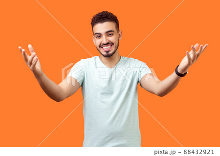 Come and give me hug. Portrait of positive generous brunette man with beard in casual white t-shirt holding hands raised and wide opened to embrace. indoor studio shot isolated on orange background Come and give me hug. Portrait of positive generous brunette man with beard in casual white t-shirt holding hands raised and wide opened to embrace. indoor studio shot isolated on orange background 88432921