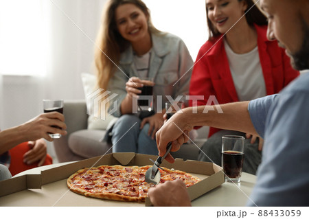 Man cutting fresh pizza on table and friends indoors, closeup Man cutting fresh pizza on table and friends indoors, closeup 88433059