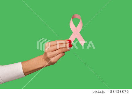 Closeup of tiny female hand with manicure holding pink ribbon, symbol of breast cancer awareness, oncological disease prevention and female healthcare. indoor studio shot isolated on green background Closeup of tiny female hand with manicure holding pink ribbon, symbol of breast cancer awareness, oncological disease prevention and female healthcare. indoor studio shot isolated on green background 88433376