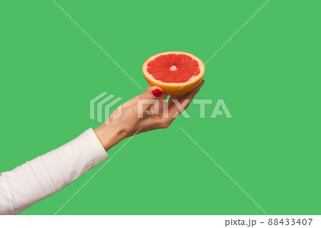 Closeup of hand holding sliced juicy grapefruit, tasty fruit for detox, natural organic vegetarian food full with vitamins, healthy diet and weightloss concept. indoor, isolated on green background Closeup of hand holding sliced juicy grapefruit, tasty fruit for detox, natural organic vegetarian food full with vitamins, healthy diet and weightloss concept. indoor, isolated on green background 88433407