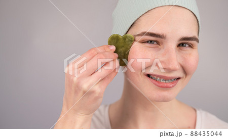 Close-up portrait of a smiling woman with braces doing home care with a gouache massager. Close-up portrait of a smiling woman with braces doing home care with a gouache massager. 88435044