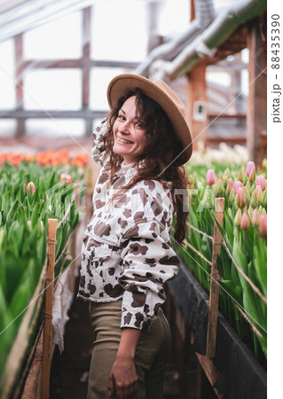 Young beautiful woman in hat posing looks at flowers in a greenhouse Tulips Young beautiful woman in hat posing looks at flowers in a greenhouse Tulips 88435390