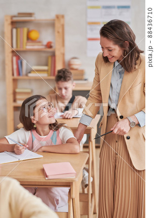 Vertical portrait of young female teacher smiling while helping children during class in school, copy space 88436710