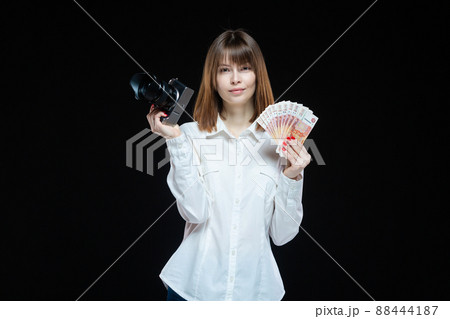 Portrait of a young woman wearing a white shirt, holding a camera and Russian rubles in her hand. The concept of a successful photographer in the Russian Federation, self-employed photographer Portrait of a young woman wearing a white shirt, holding a camera and Russian rubles in her hand. The concept of a successful photographer in the Russian Federation, self-employed photographer 88444187