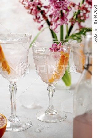 Pink cocktail with orange slice and ice cubes in crystal glasses with pink spring flowers Hyacinth. Alcoholic, refreshing party drink. Pink cocktail with orange slice and ice cubes in crystal glasses with pink spring flowers Hyacinth. Alcoholic, refreshing party drink. 88447008