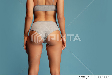 Studio shot of slim, sportive female body in gray comfortable underwear isolated over blue background. Sportive bottocks, legs 88447443