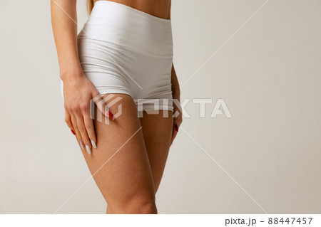 Cropped studio shot of slim, sportive female body in white comfortable underwear isolated over gray background Cropped studio shot of slim, sportive female body in white comfortable underwear isolated over gray background 88447457