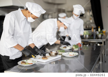 al group of cooks finishing main courses while working together in the kitchen al group of cooks finishing main courses while working together in the kitchen 88449261